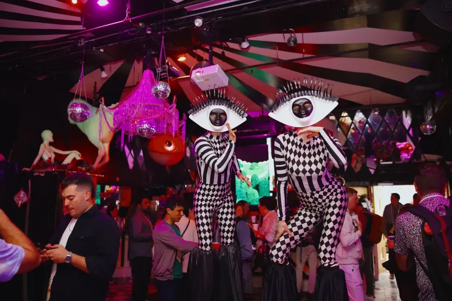 Stilt walkers in checkerboard suits and giant eye masks working the party
