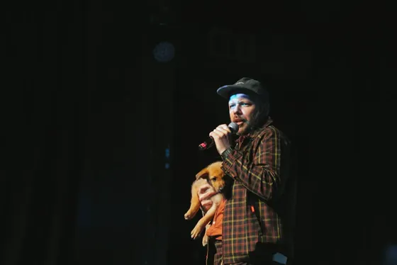 Host on stage with a mic, holding a puppy mid-set