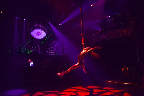Aerialist spinning on a rope above the crowd, beside the giant lit eye